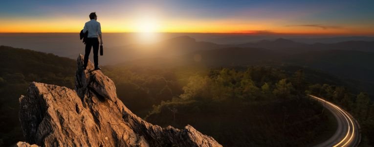 Businessman on Top of a Mountain Looking at Sunrise