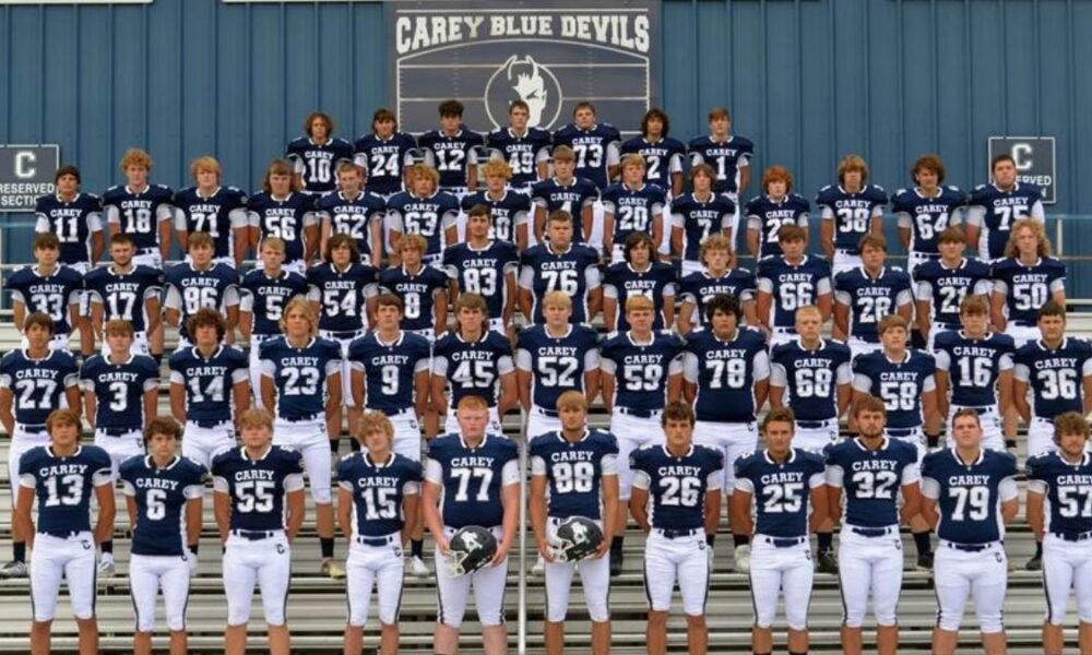 Carey High School Blue Devils football players standing on stadium seats with the "Carey Blue Devil" logo prominently displayed behind them.