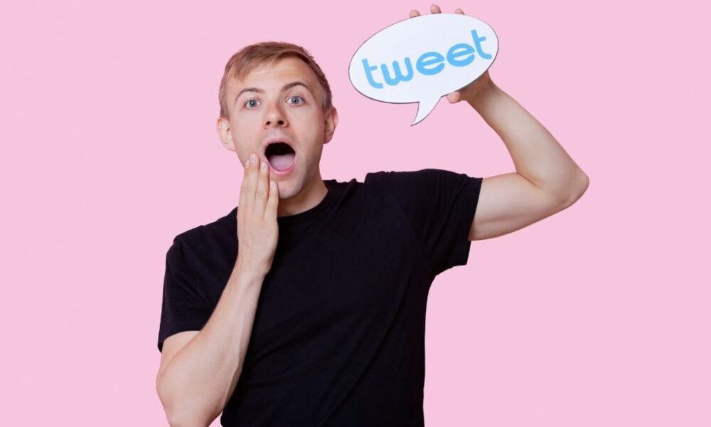 Portrait of surprised young man holding tweet bubble against pink background