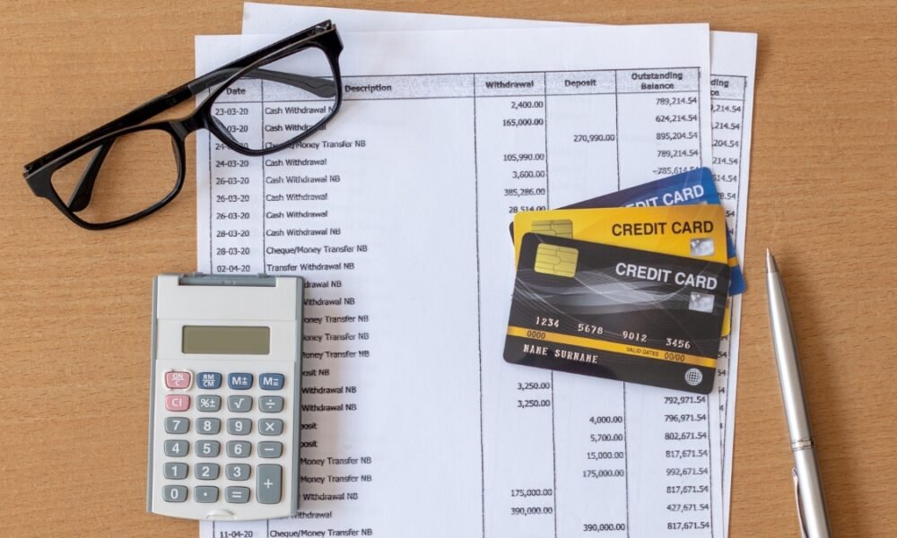 A calculator, some visa cards, Glasses and Bank statement placed on a table together