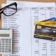 A calculator, some visa cards, Glasses and Bank statement placed on a table together