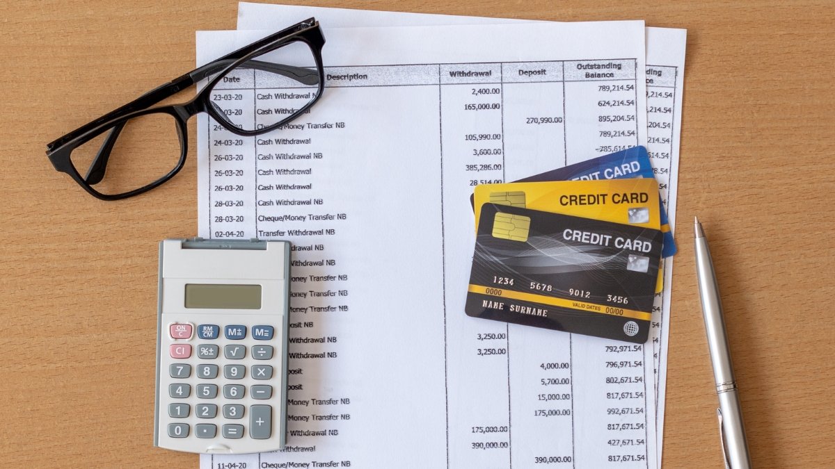 A calculator, some visa cards, Glasses and Bank statement placed on a table together