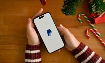 A female hand holding a smartphone with PayPal logo over table w