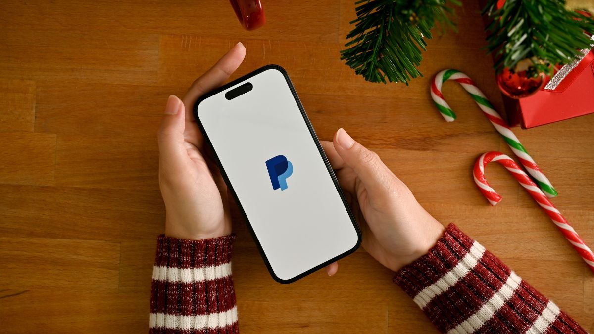 A female hand holding a smartphone with PayPal logo over table w