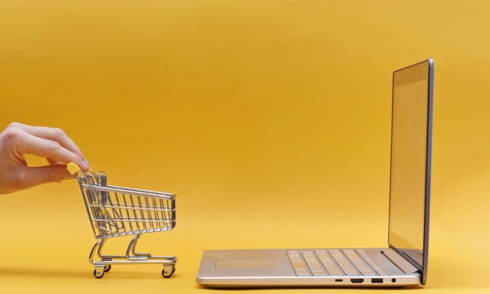 Hand Holding Mini Shopping Trolley near the Opened Laptop