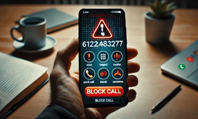 A smartphone screen showing an incoming call from the number 6122483277 tel, with a red warning triangle symbol indicating a potential scam or fraudulent call. The phone is held in a hand, and the background shows a muted office setting.